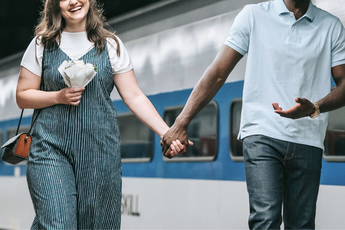 Expecting couple holding hands near a train for a romantic winter babymoon trip.
