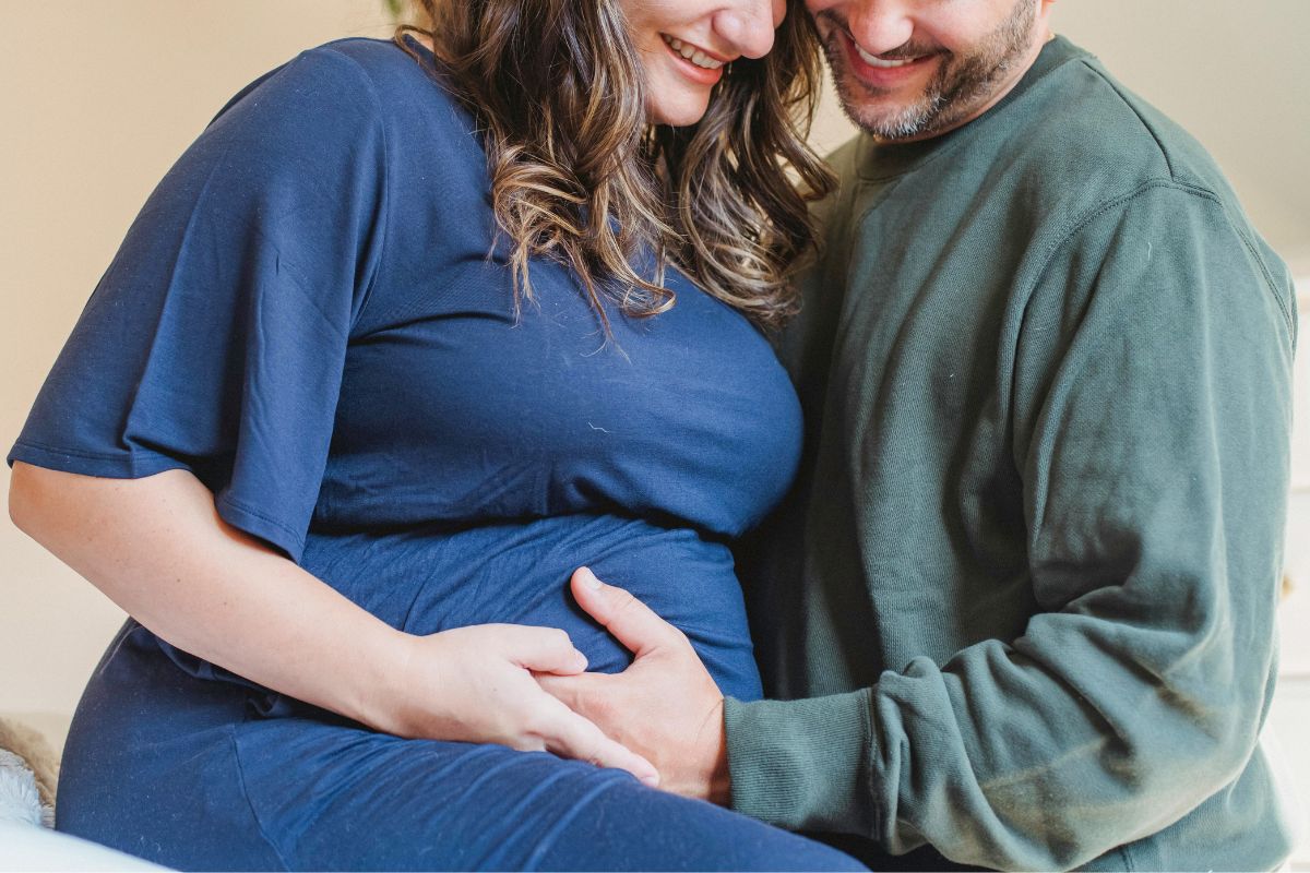 Pregnant couple cuddling together during a cozy winter babymoon staycation at home.