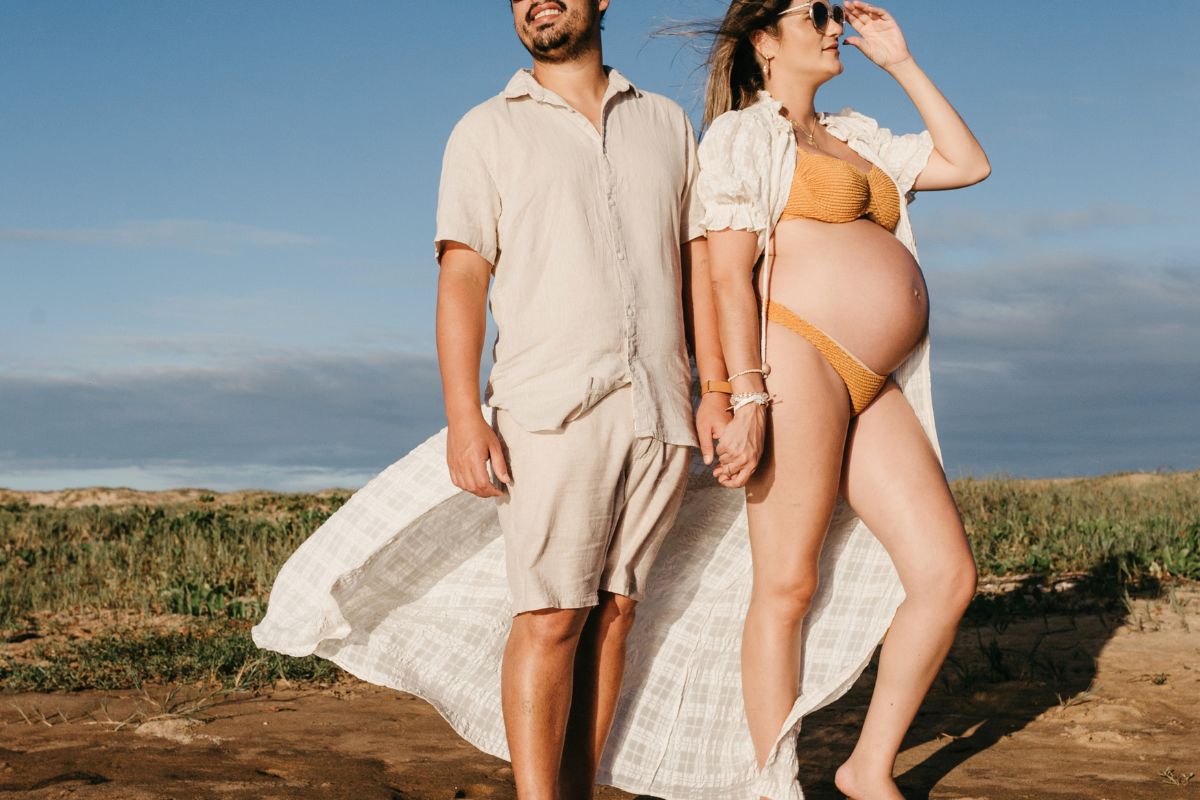 Expecting couple walking on the beach during a warm winter babymoon escape.