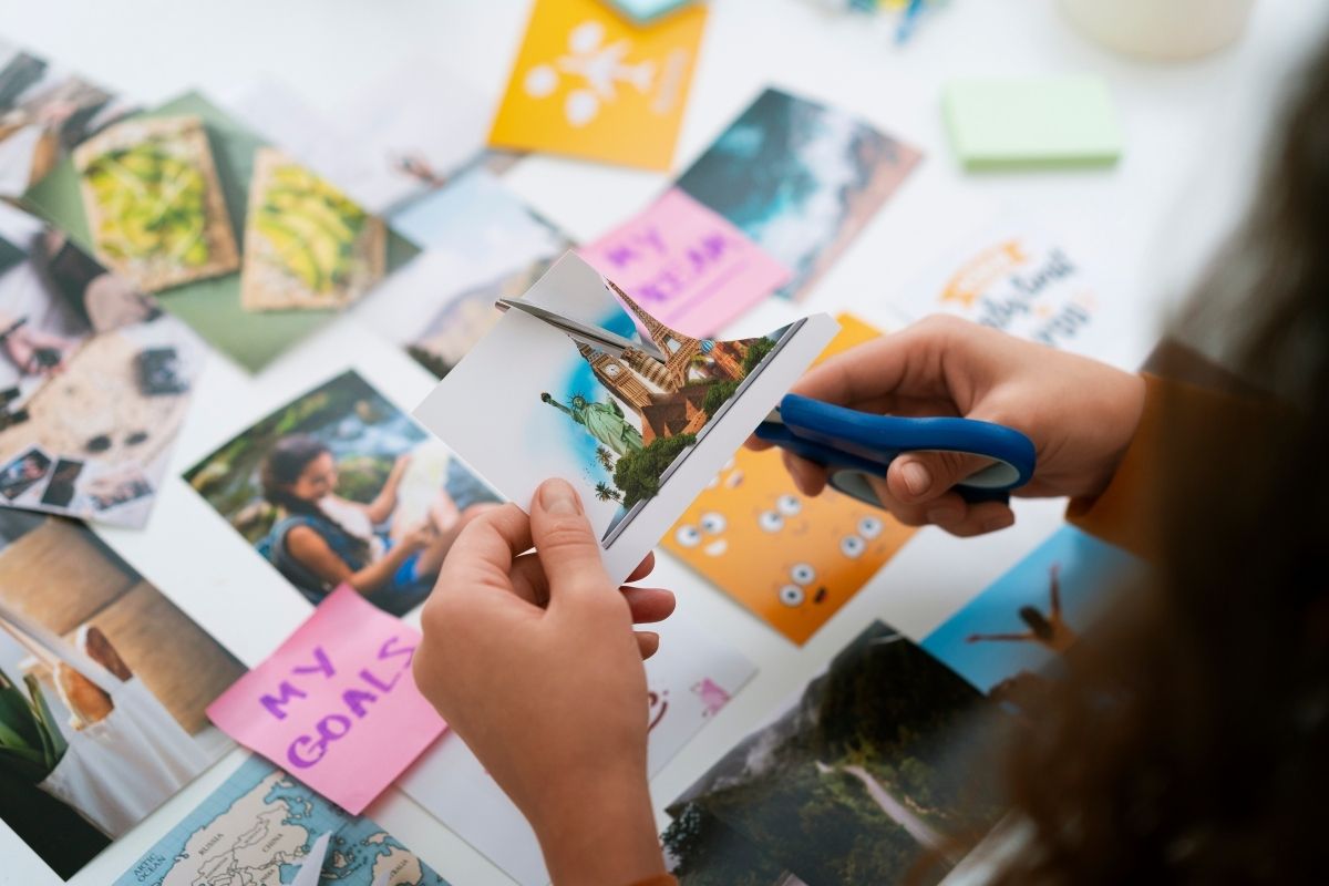 Hands cutting printed pictures with scissors for a creative collage project on a table covered with photos and colorful notes.