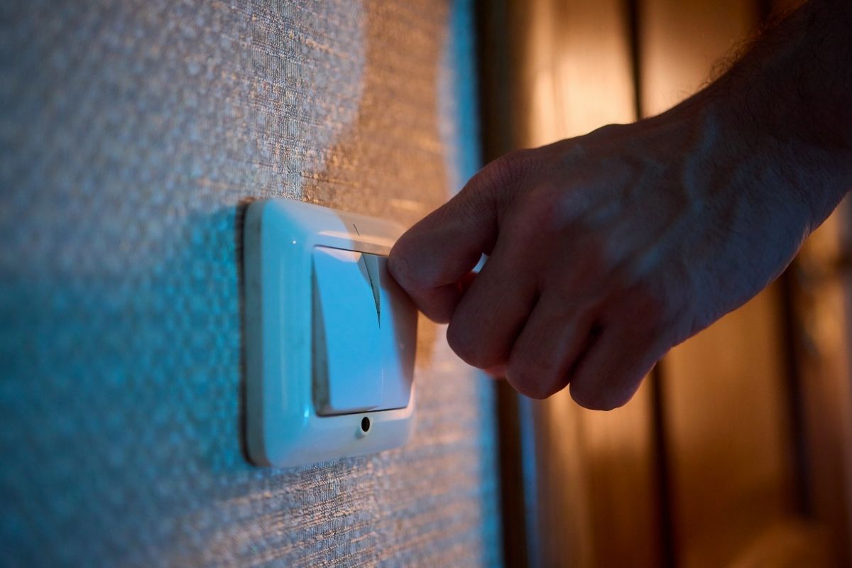 Close-up of a hand turning off a wall light switch, creating a calm, dimly lit environment for a toddler's bedtime routine.