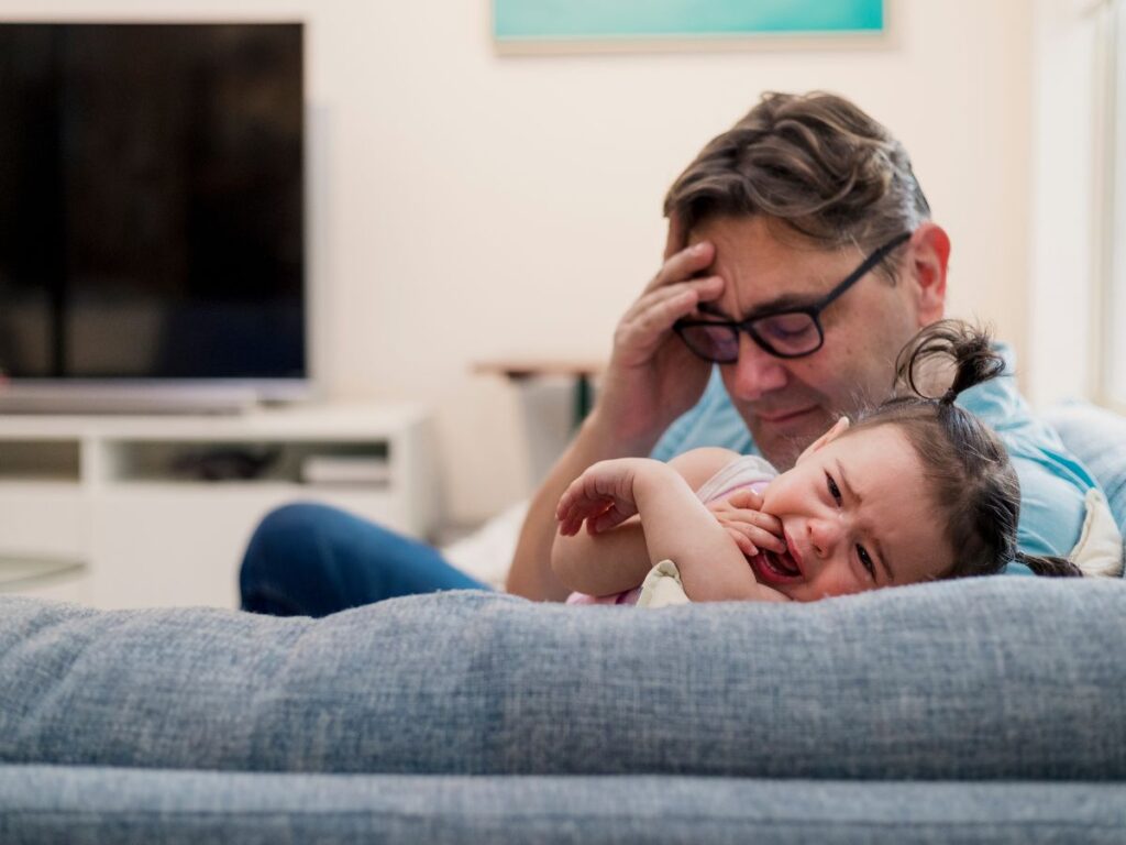 Frustrated father and his crying baby on the couch