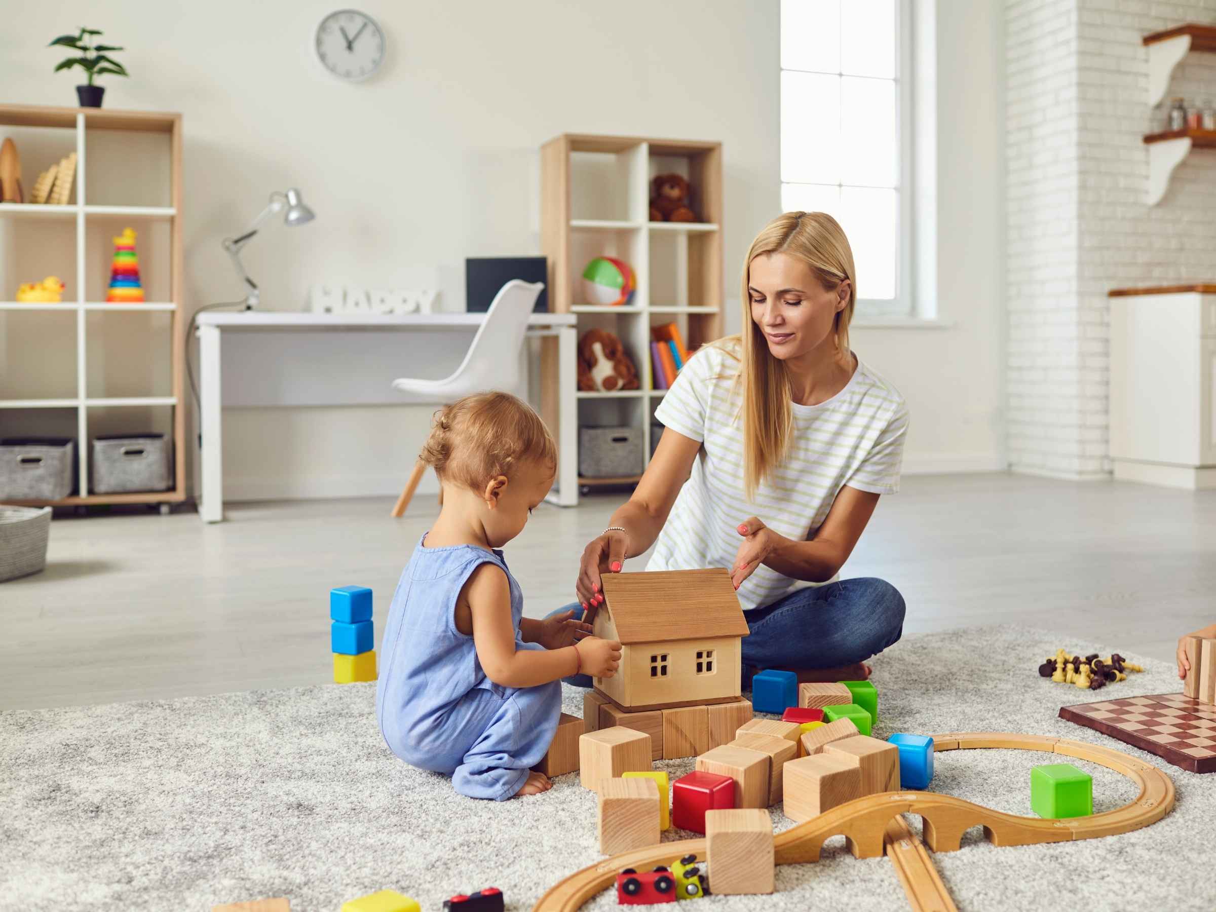 mother and child playing with wooden blocks and a toy house. on the carpeted floor