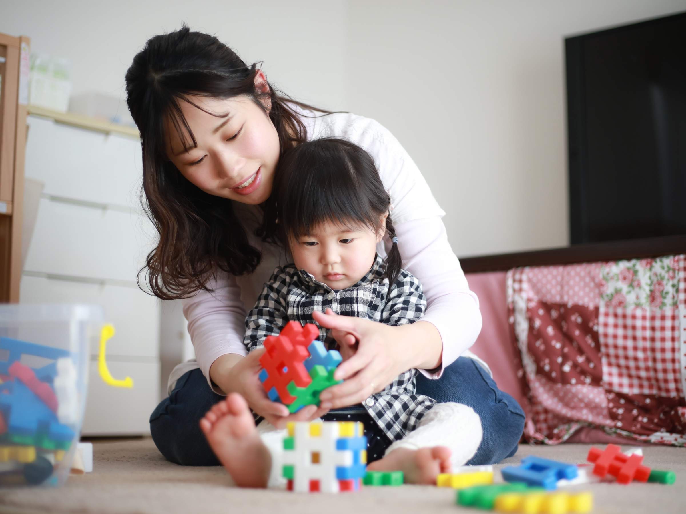 mother sitting on the floor with her toddler, playing with colorful interlocking plastic blocks