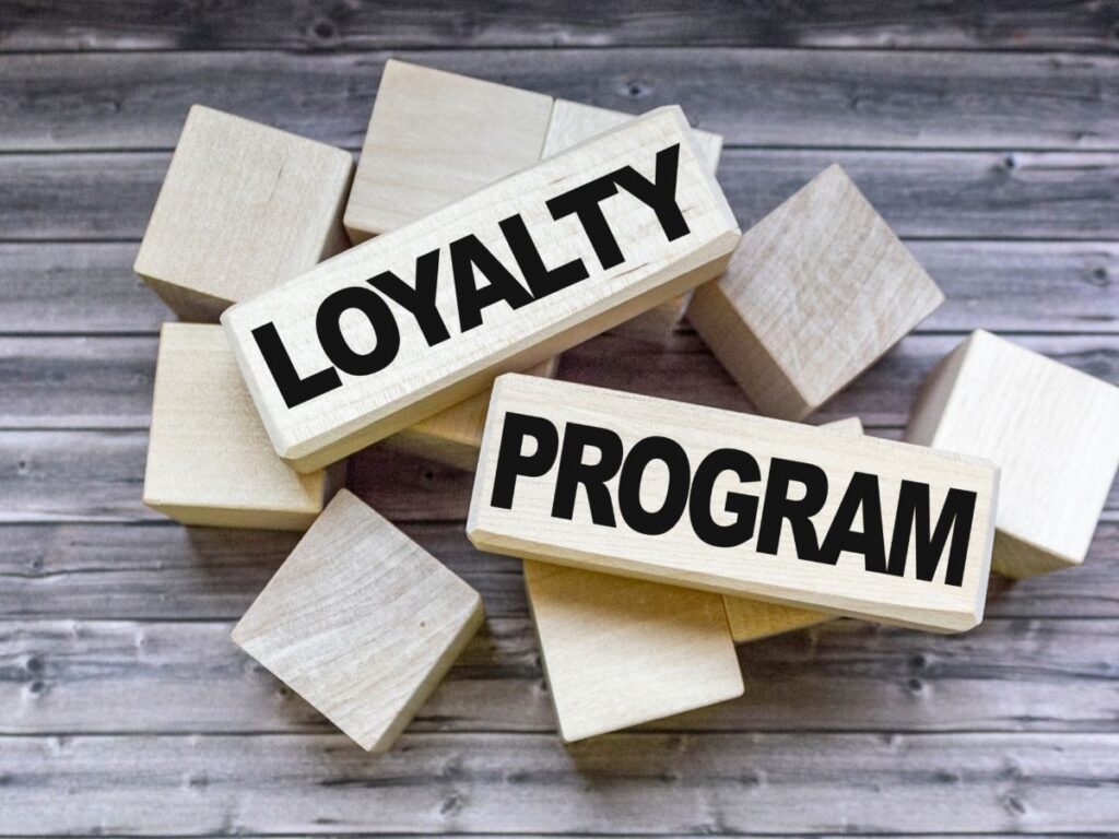 Wooden blocks arranged on a wooden surface, with two larger blocks prominently displaying the words 'LOYALTY' and 'PROGRAM' in bold black letters
