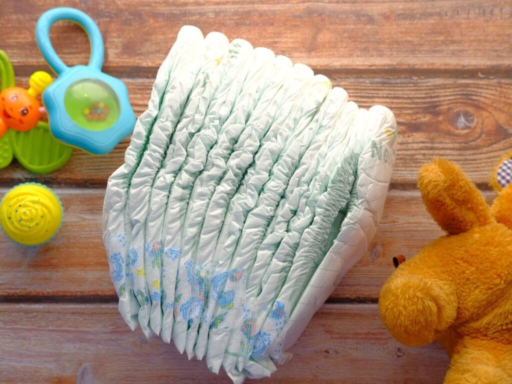 baby diapers neatly placed on a wooden surface, surrounded by colorful baby toys