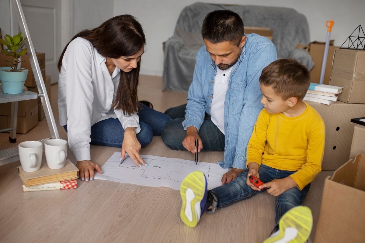 Parents sitting on the floor with their young son, reviewing plans and discussing home arrangements together.