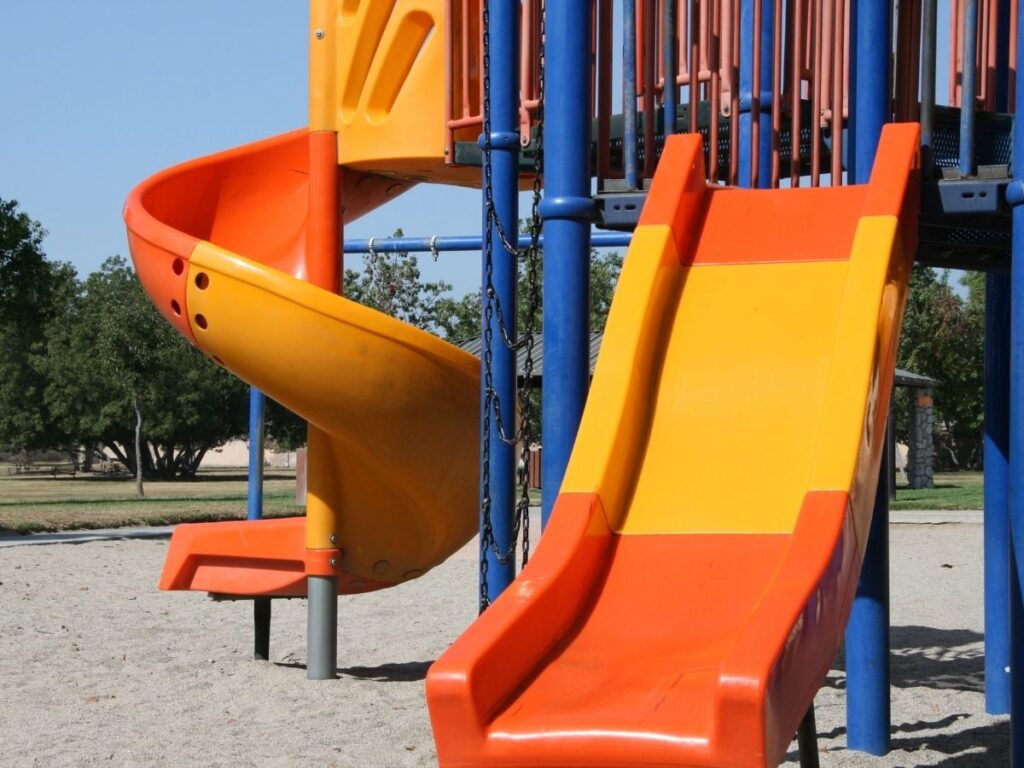 Playground structure with a straight orange and yellow slide and a spiral orange slide