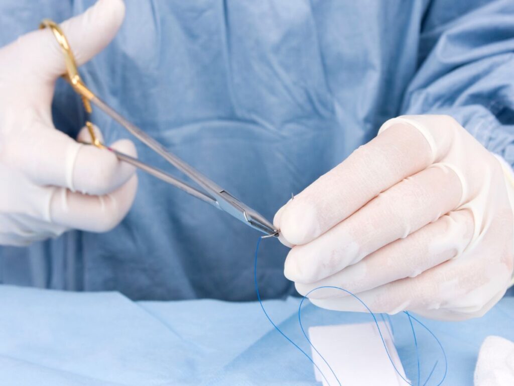 Surgeon in blue surgical gown and gloves handling suture thread