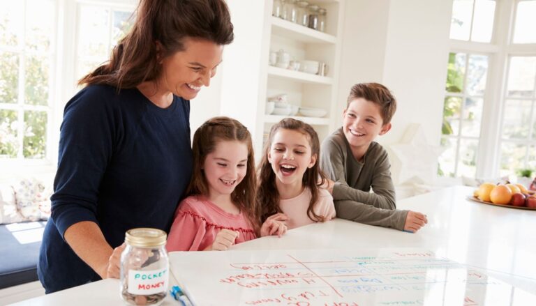 mother with her two young daughters and son organizing chores on a small whiteboard in a kitchen, with a labeled 'Pocket Money' jar nearby