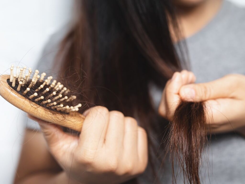 Woman loosing her hair, holding a hairbrush with strands of hair tangled in the bristles