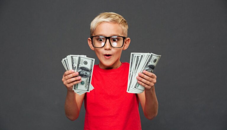 Young boy holding stacks of cash with an excited expression.