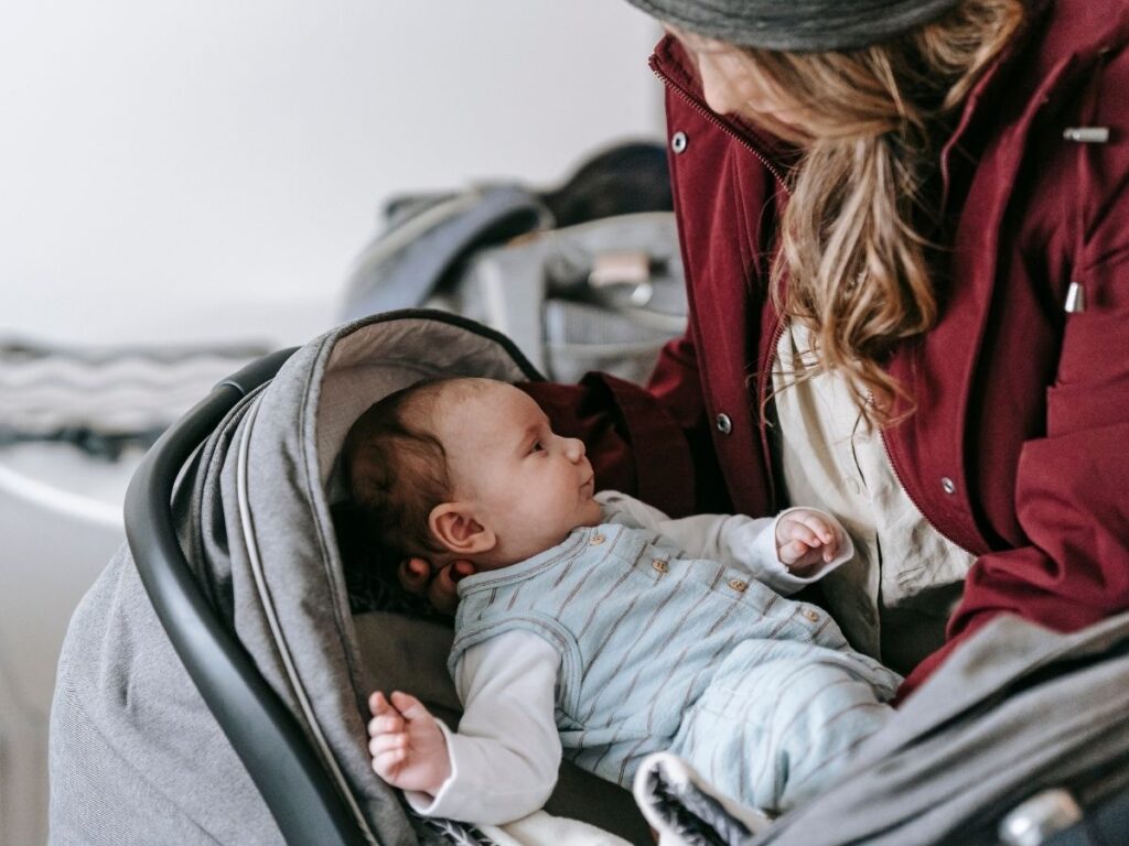a lady in a maroon jacket gently putting a baby in a stroller