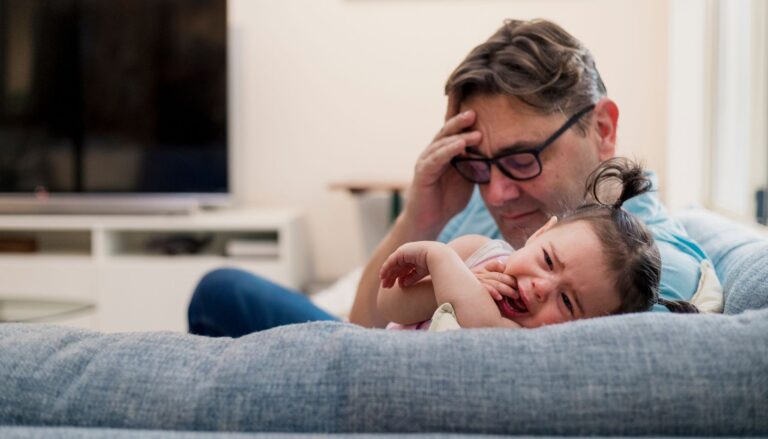 Frustrated father and his crying baby on the couch
