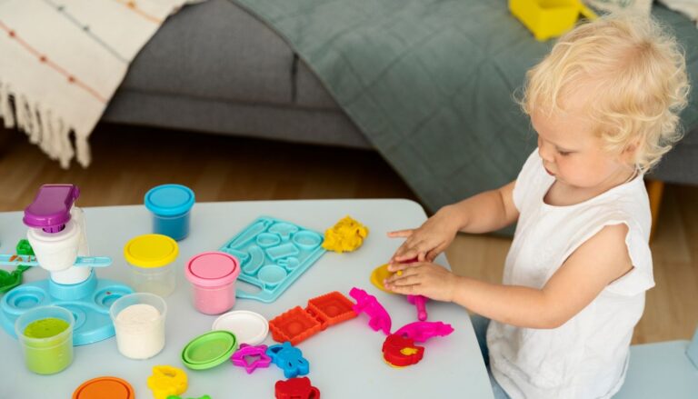 Toddler playing with colorful modeling dough, plastic molds, and tools at a small table.