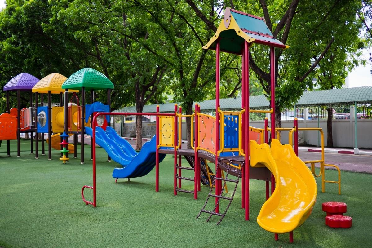 Colorful outdoor playground with slides, climbing structures, and a rubber safety surface.