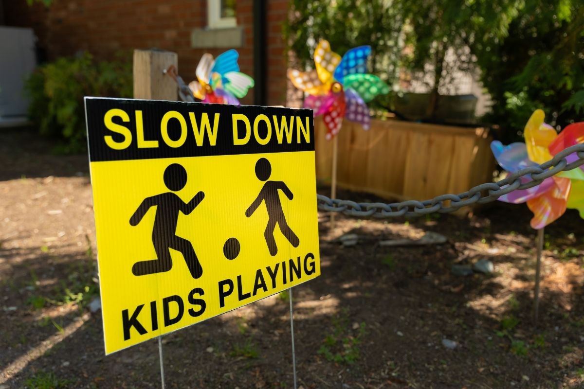 Yellow “Slow Down Kids Playing” safety sign displayed near an outdoor play area.