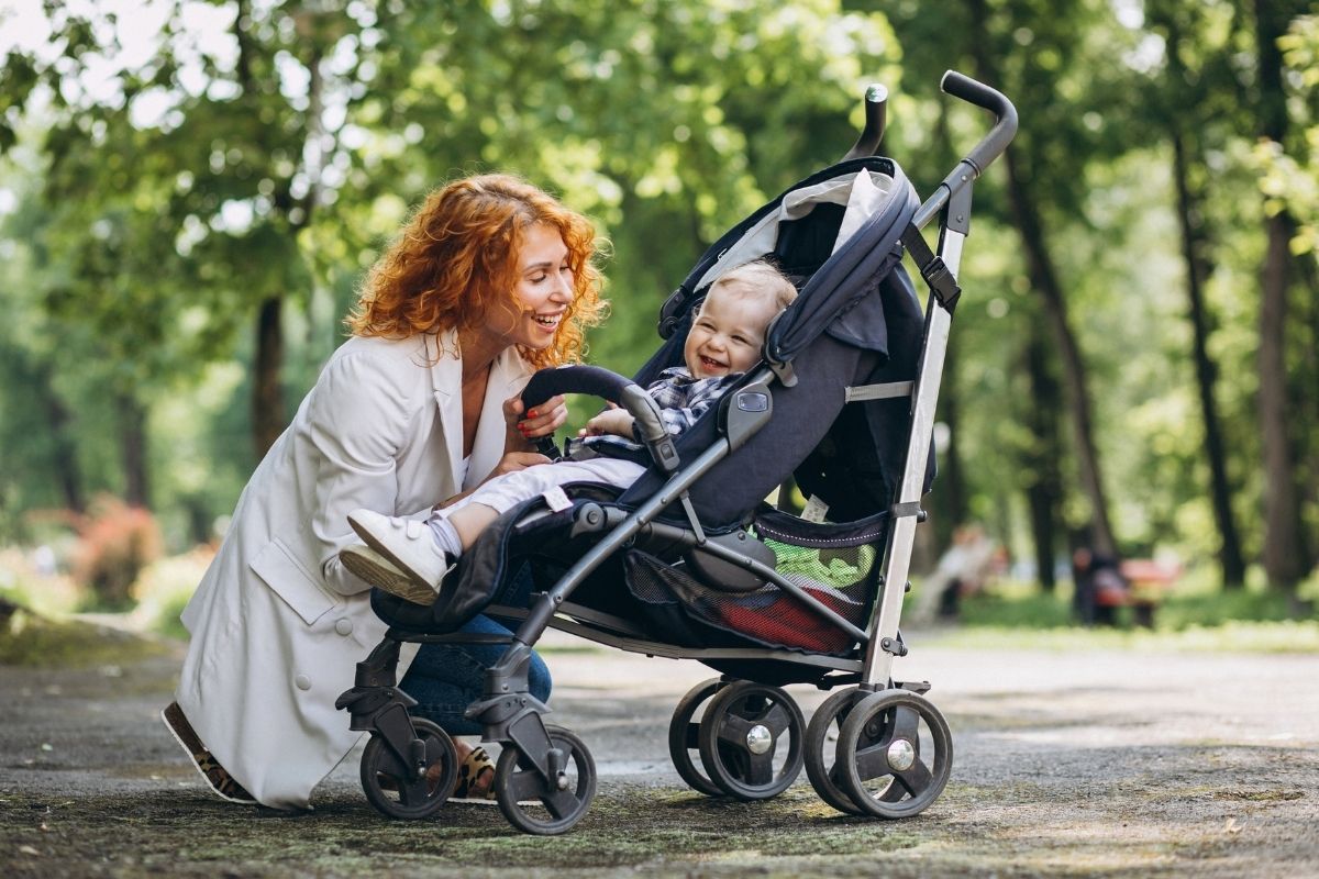 Woman with a child in a lightweight stroller while walking through a park.