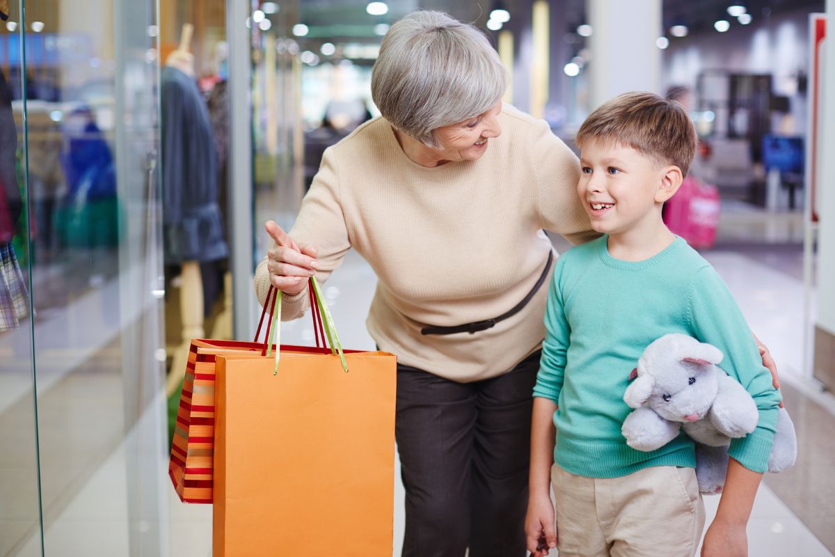 Woman shopping with a young boy carrying a stuffed toy in a shopping mall.