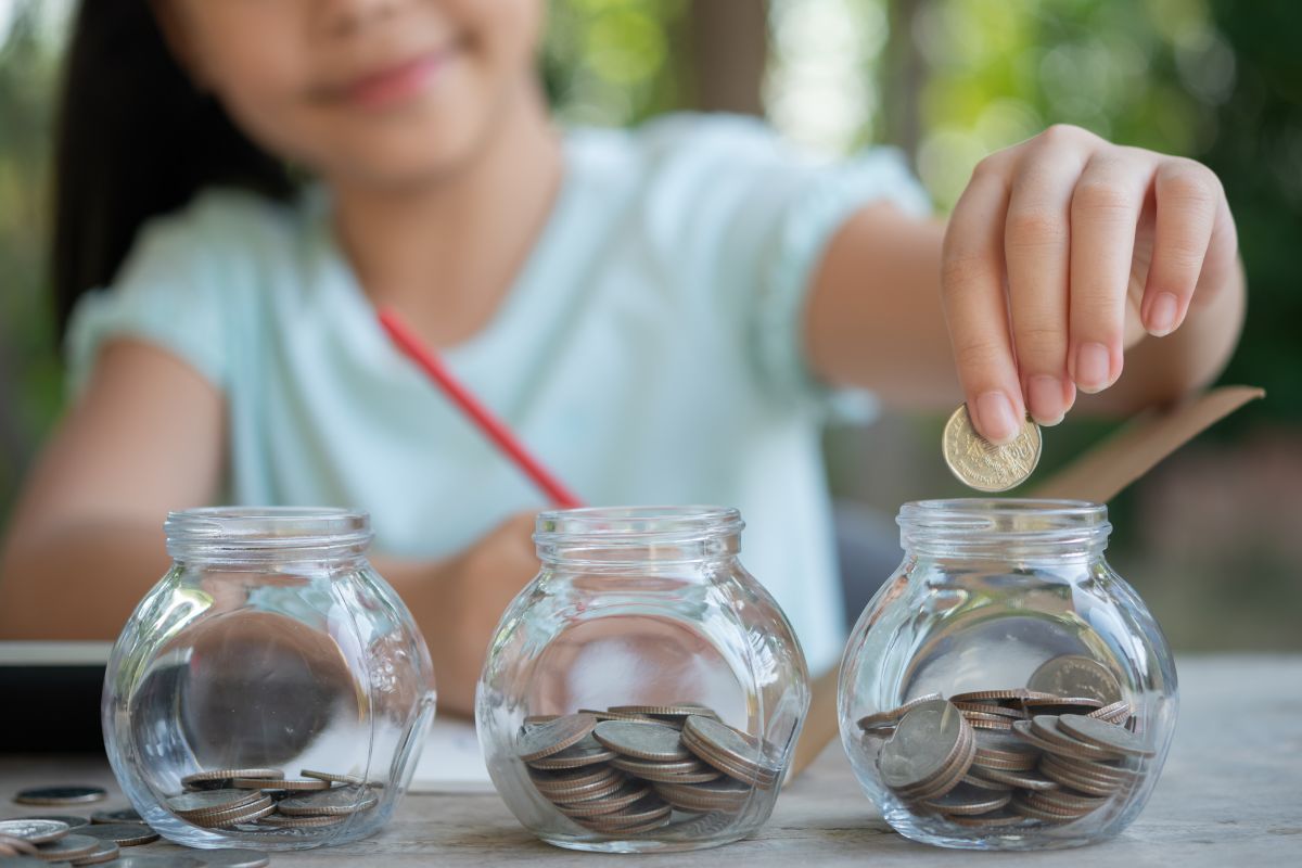 Young girl placing coins into separate glass jars to organize her savings.