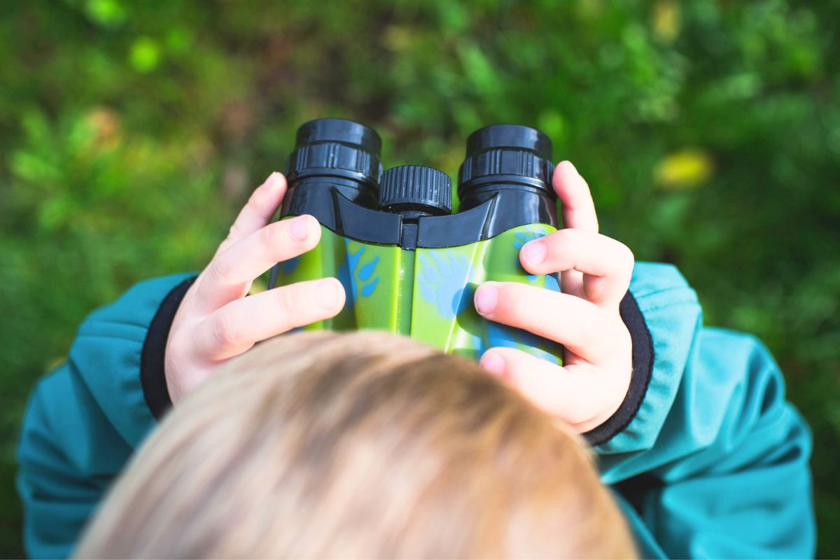 Child using binoculars exploring nature during a fun camping trip with kids.