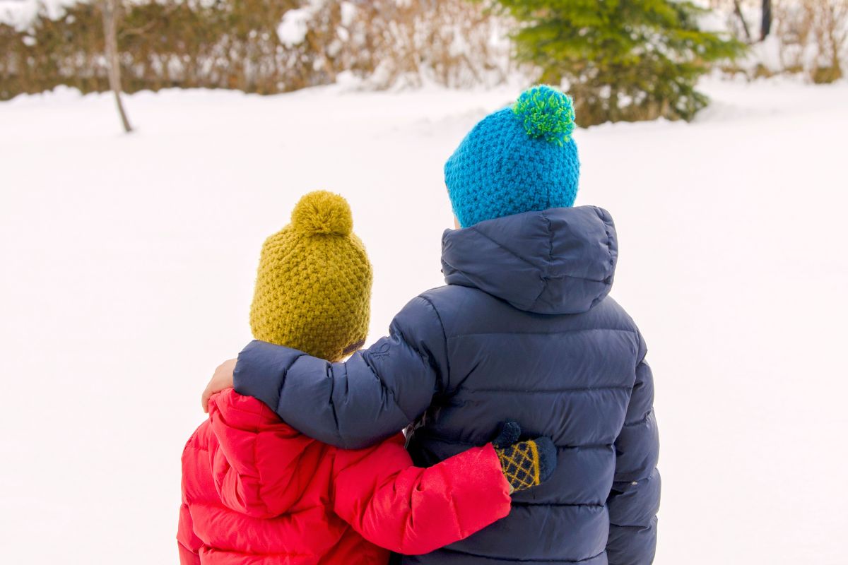 Kids in warm winter jackets walking in snow, showing how to stay warm during winter travel with kids.