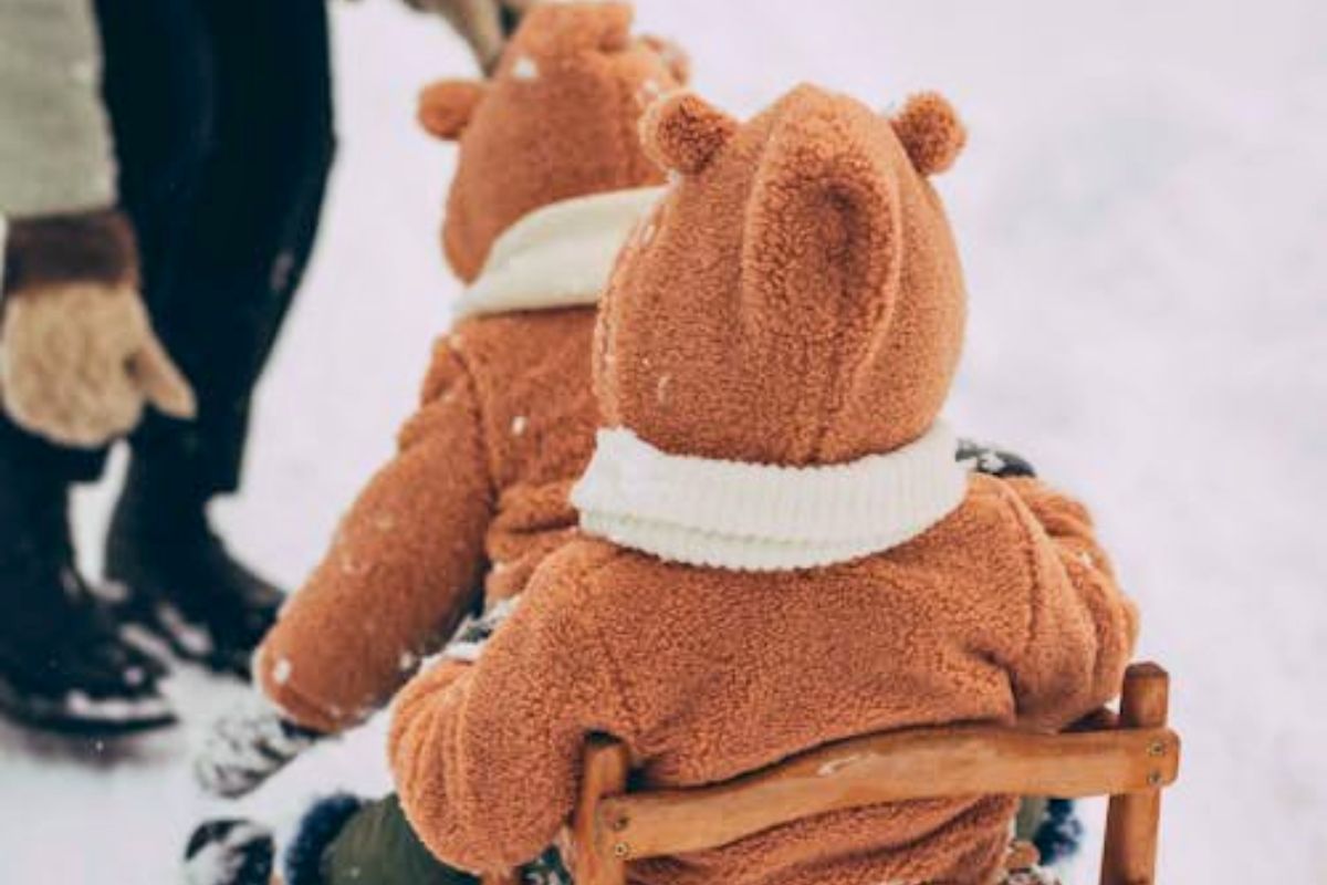 Toddlers in cozy winter outfits sitting on a sled, illustrating smart packing for winter travel with kids.