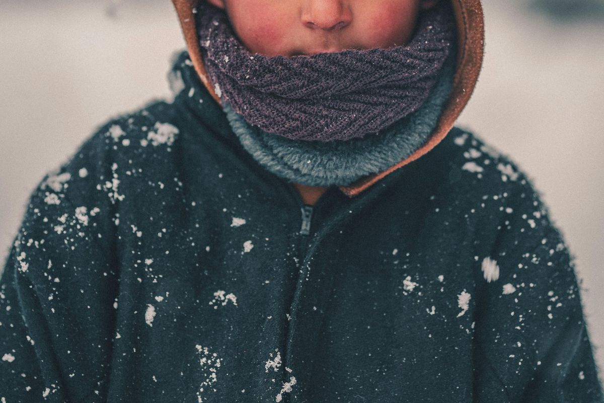 Child bundled in layers with scarf and hood in snowy weather, demonstrating how to stay warm in winter travel.