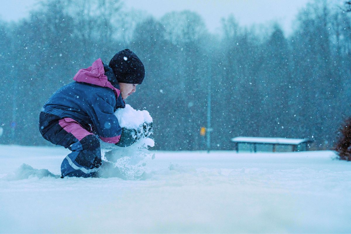 Kid playing in snow wearing insulated winter clothing, showing proper layering for winter travel with kids.