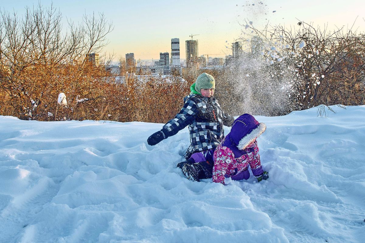 Kids playing in deep snow with winter gear, highlighting staying warm and prepared during family winter travel.