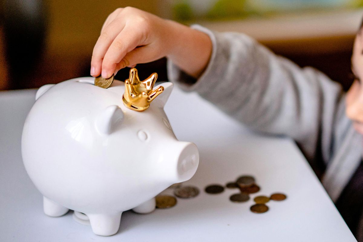 Child putting coin in piggy bank learning basic budgeting for kids.