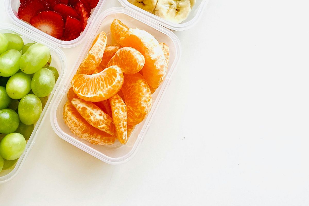 Containers with grapes, strawberries, orange slices, and bananas, showing healthy toddler snacks for road trips.