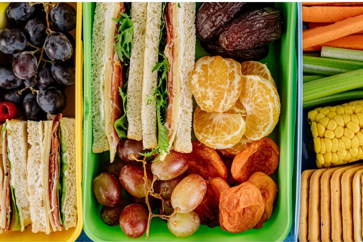 Lunchbox with sandwiches, grapes, crackers, and veggies, a variety of toddler-friendly snacks for long car rides.