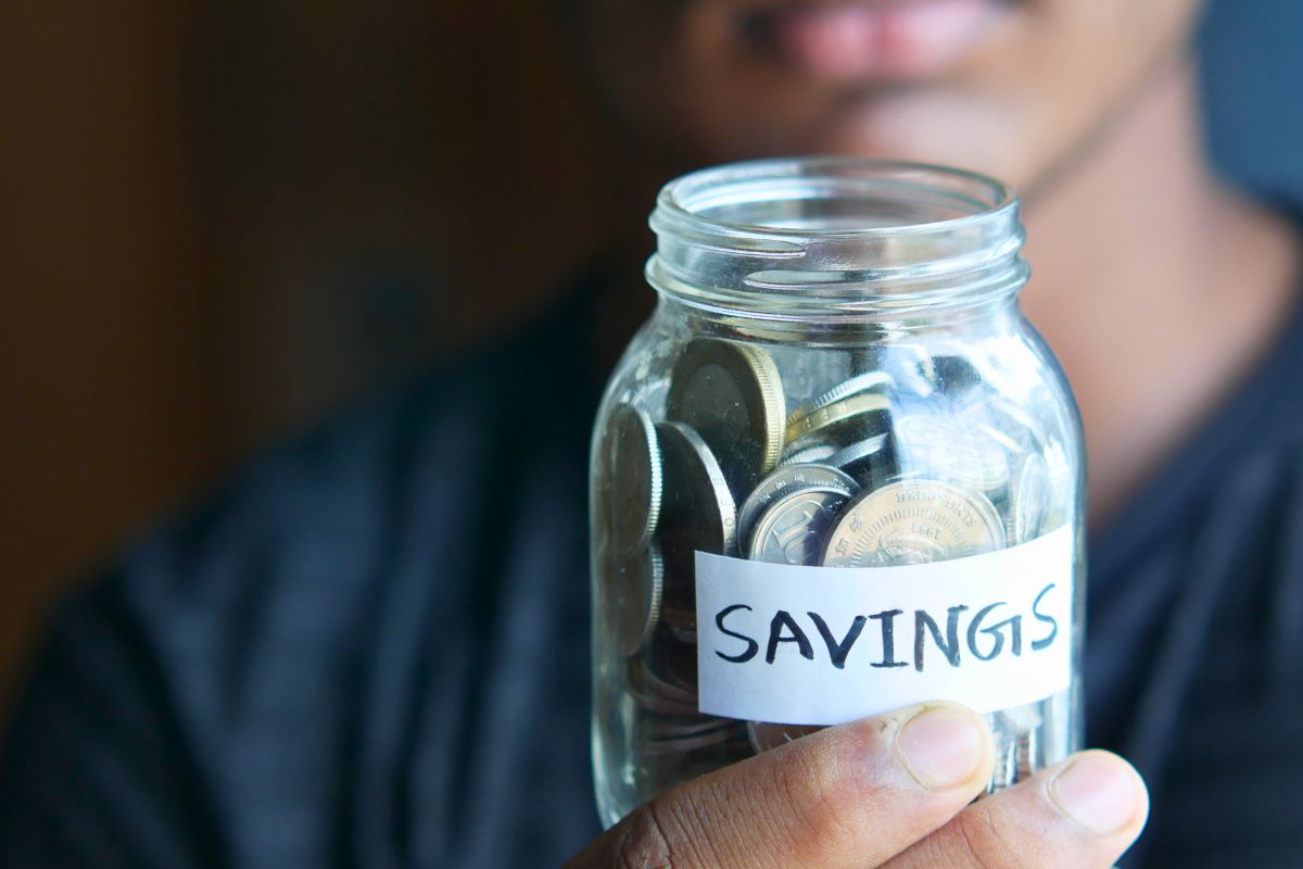 Child holding a jar of coins labeled savings, representing saving money for kids and building patience.