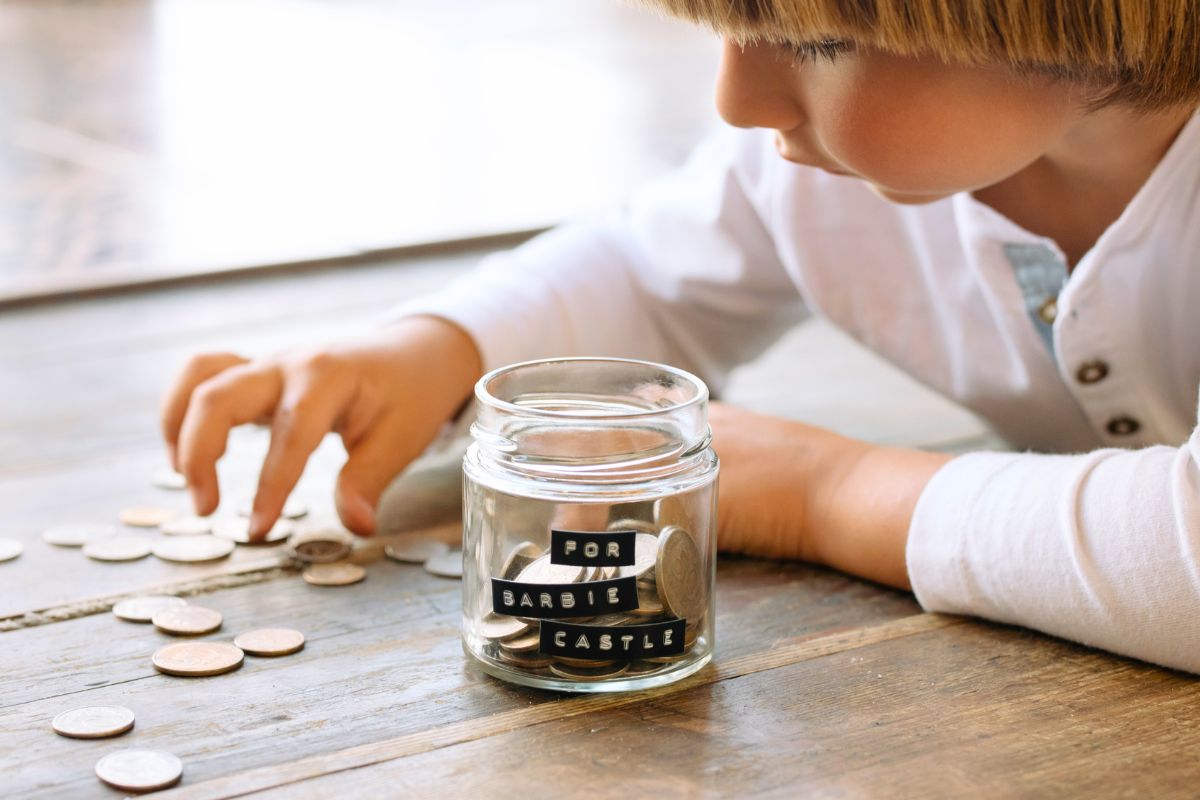 Child counting coins next to a labeled savings jar, tracking progress toward buying a toy.