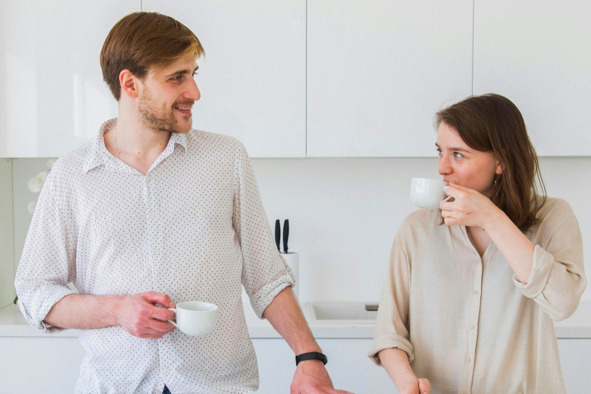 Couple sharing a calm conversation over coffee in a bright kitchen.