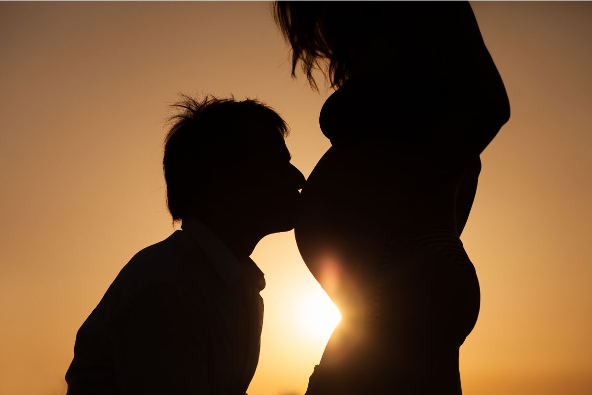 Silhouette of a man kissing a pregnant woman's baby bump.