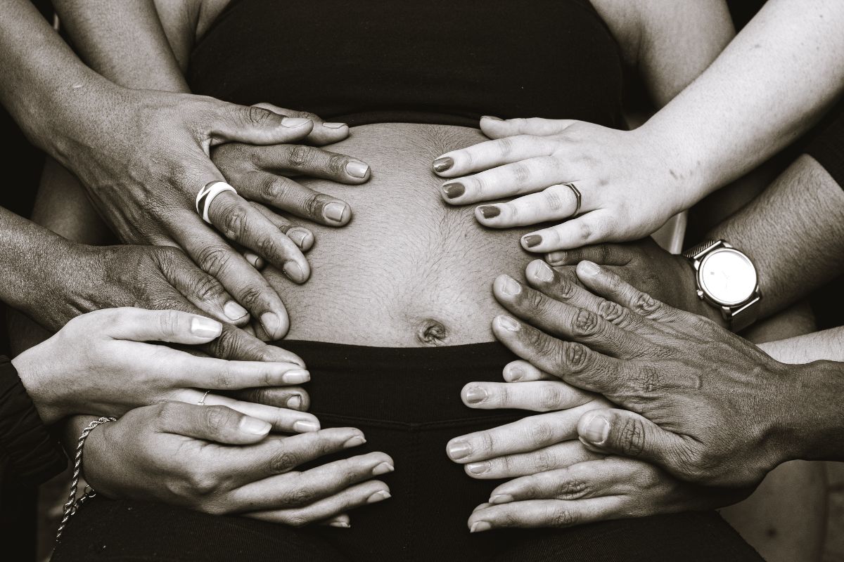 Several hands gently resting on a pregnant woman's baby bump, symbolizing support during pregnancy.