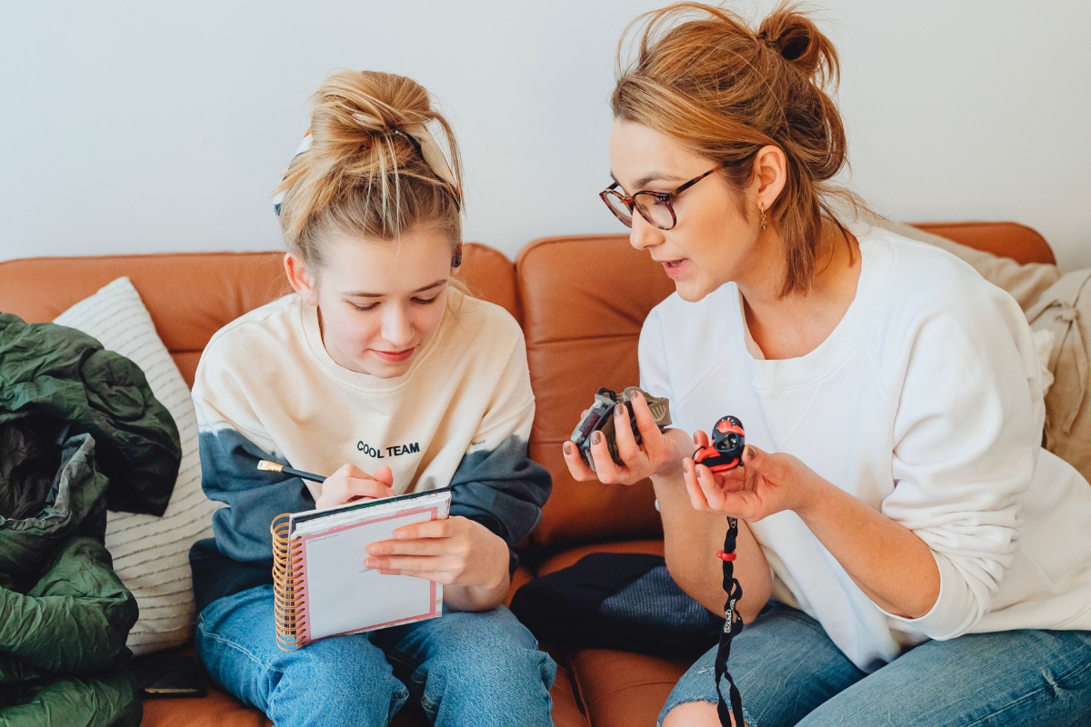 Mother helping her teenage daughter plan school tasks in a notebook.