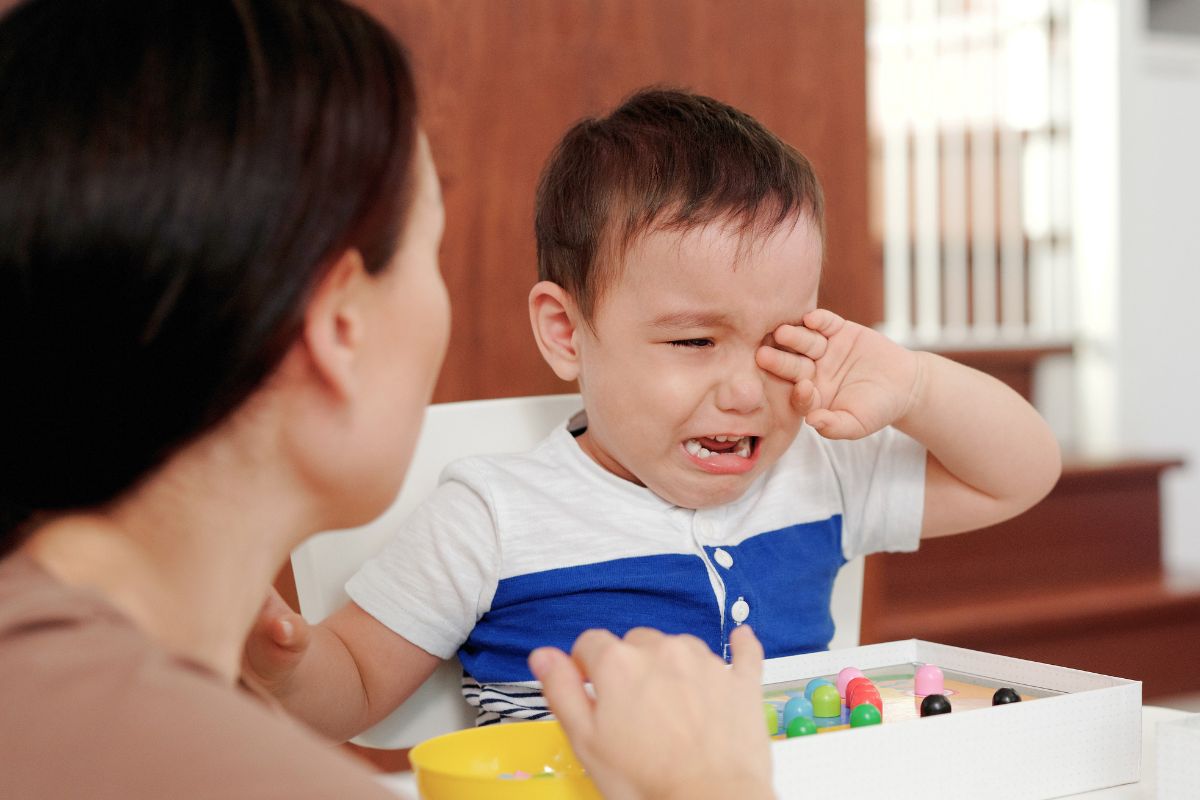 Parent sitting beside a crying toddler during a difficult emotional meltdown at home.