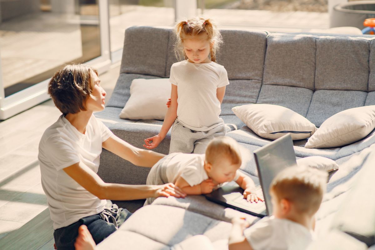 Parent balancing work and caring for three young children at home during a busy day.