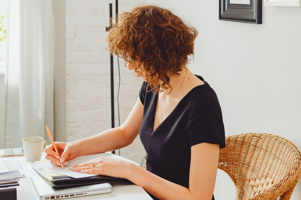 Woman writing notes beside a laptop while planning and organizing family tasks at home.