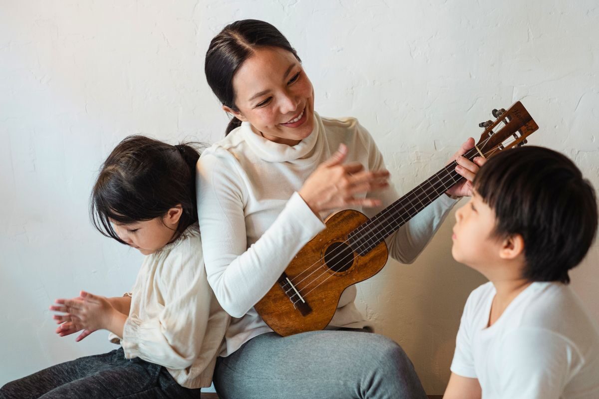 Mother playing the ukulele with her children, showing how parents can reconnect with themselves through hobbies while raising a family.