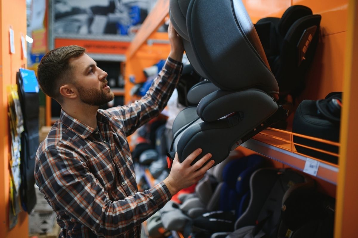 Man shopping for a child car seat in a store with rows of car seats on display.
