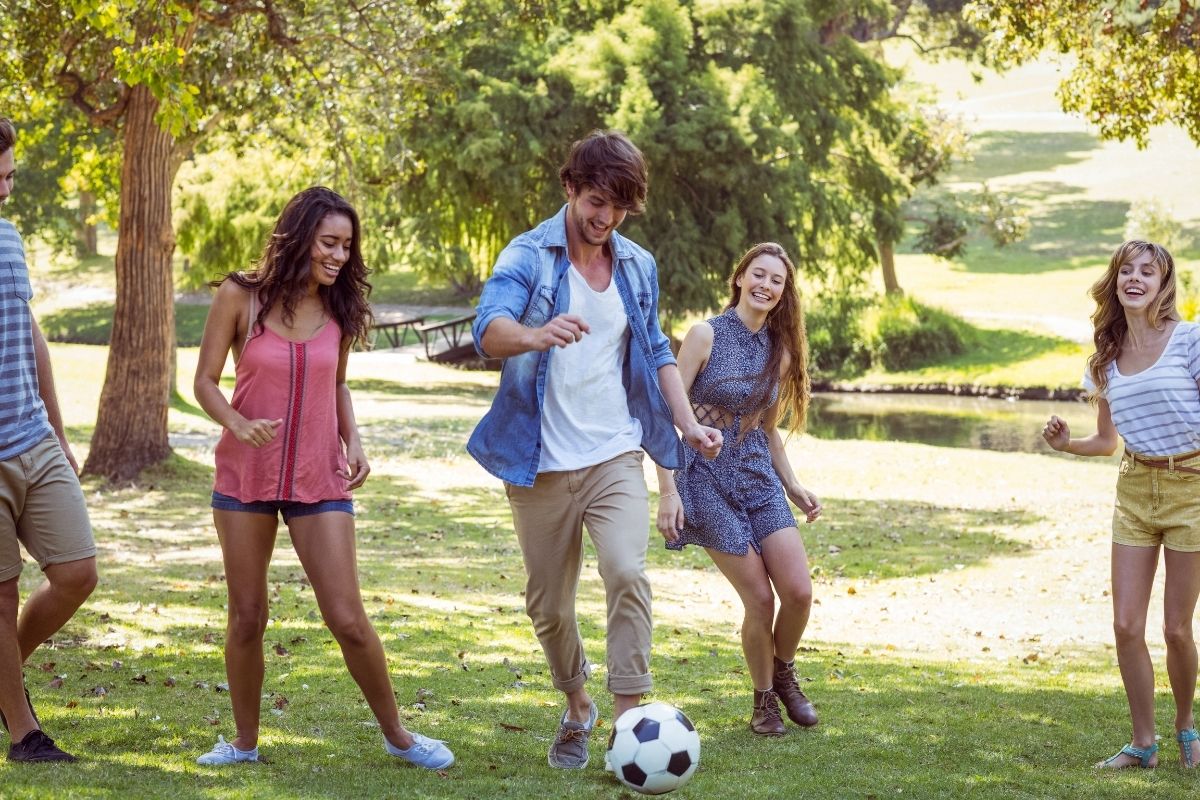 Group of friends playing soccer together on a sunny day in a green park.